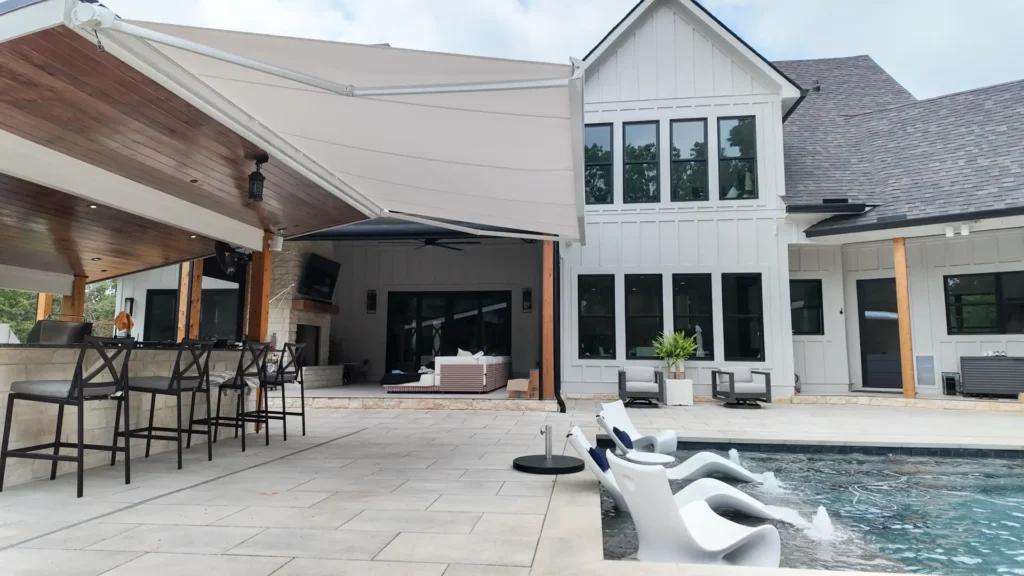 KE Domina Retractable Awning extending from the outdoor kitchen pavilion toward the pool